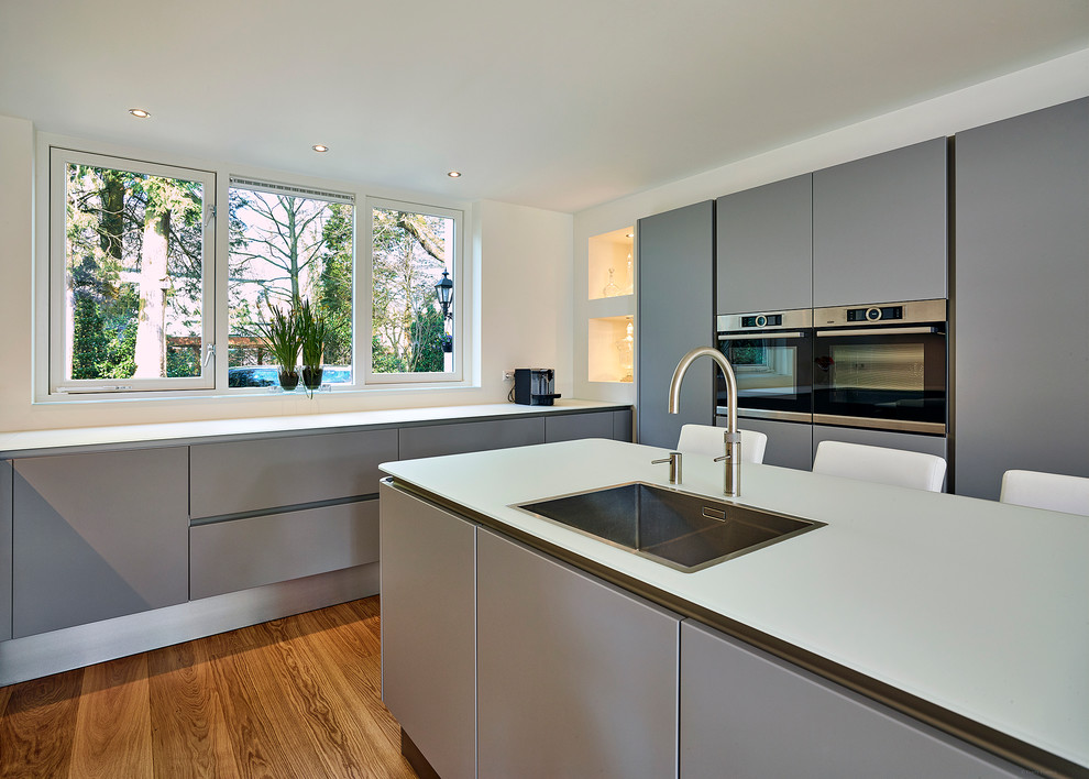 Foto di una grande cucina design con lavello da incasso, ante lisce, ante grigie, top in vetro, elettrodomestici neri e pavimento in legno massello medio