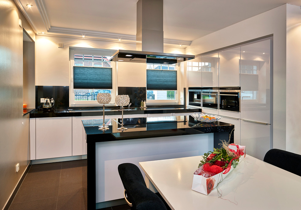 Immagine di una cucina contemporanea di medie dimensioni con lavello da incasso, ante lisce, ante bianche, top in granito, paraspruzzi nero e elettrodomestici neri