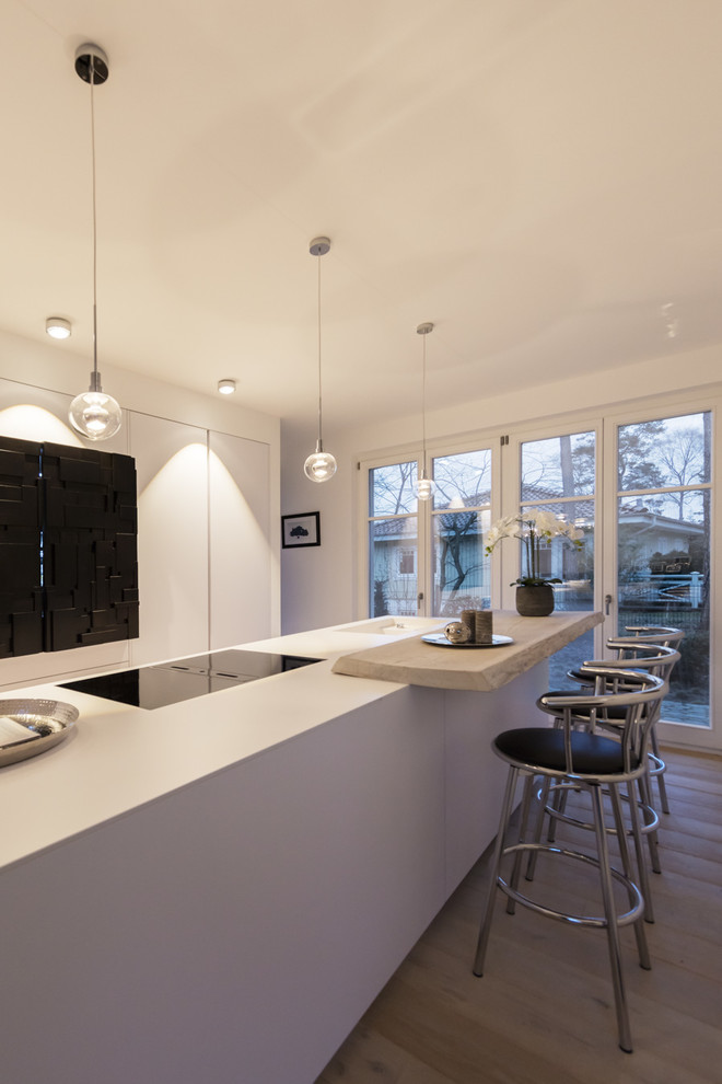 На фото: параллельная кухня-гостиная среднего размера в стиле модернизм с плоскими фасадами, белыми фасадами, островом, черной техникой, светлым паркетным полом, серым полом и белой столешницей с