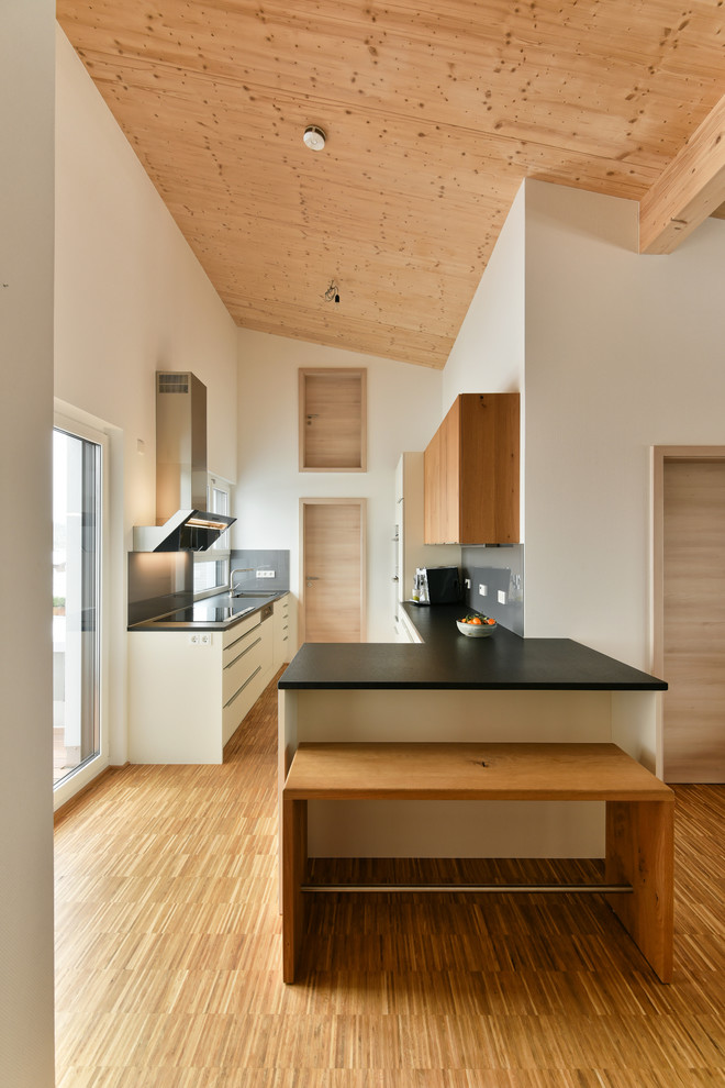 Design ideas for a medium sized contemporary galley kitchen in Stuttgart with an integrated sink, flat-panel cabinets, medium wood cabinets, grey splashback, black appliances, medium hardwood flooring and a breakfast bar.