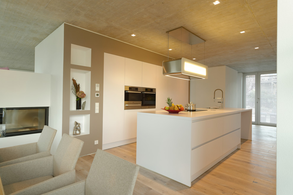 Idéer för ett stort modernt kök, med en integrerad diskho, släta luckor, vita skåp, rostfria vitvaror, ljust trägolv och en köksö