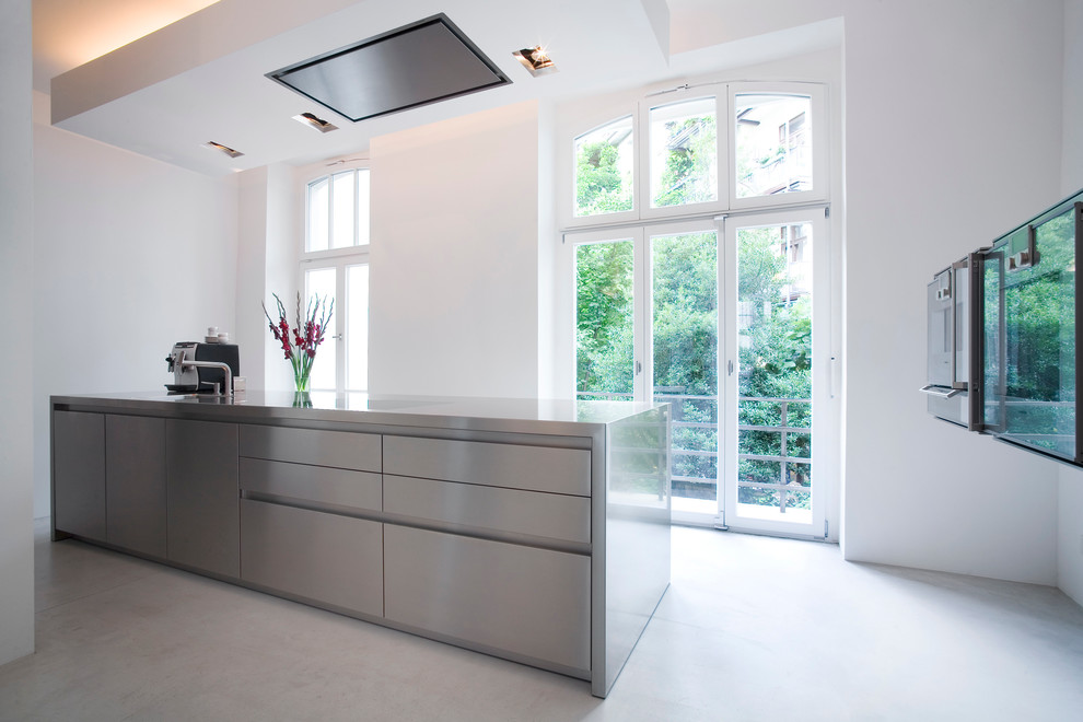 Modern inredning av ett stort linjärt kök, med en enkel diskho, släta luckor, skåp i rostfritt stål, bänkskiva i rostfritt stål, en köksö, svarta vitvaror och linoleumgolv