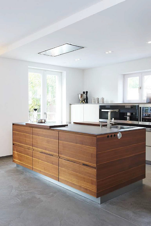 На фото: параллельная кухня-гостиная среднего размера в современном стиле с плоскими фасадами, коричневыми фасадами, белым фартуком, бетонным полом и островом с