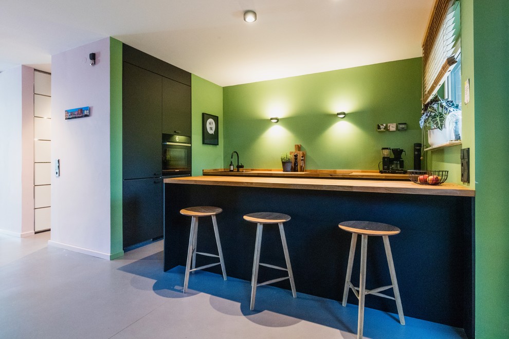 Esempio di una cucina contemporanea di medie dimensioni con lavello da incasso, ante nere, top in legno, paraspruzzi verde, elettrodomestici neri, pavimento in linoleum, pavimento grigio e top marrone