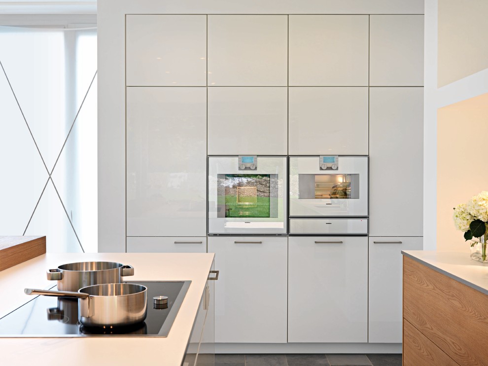 Modelo de cocina contemporánea con armarios con paneles lisos, puertas de armario blancas, electrodomésticos blancos y suelo de pizarra