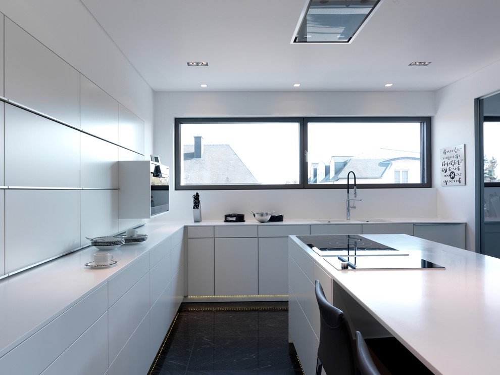 Modern inredning av ett avskilt, stort l-kök, med en dubbel diskho, släta luckor, vita skåp, integrerade vitvaror, skiffergolv och en köksö