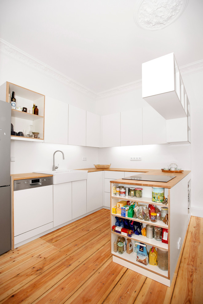 Inspiration for a medium sized contemporary u-shaped open plan kitchen in Berlin with a belfast sink, flat-panel cabinets, white cabinets, medium hardwood flooring, a breakfast bar, wood worktops and integrated appliances.