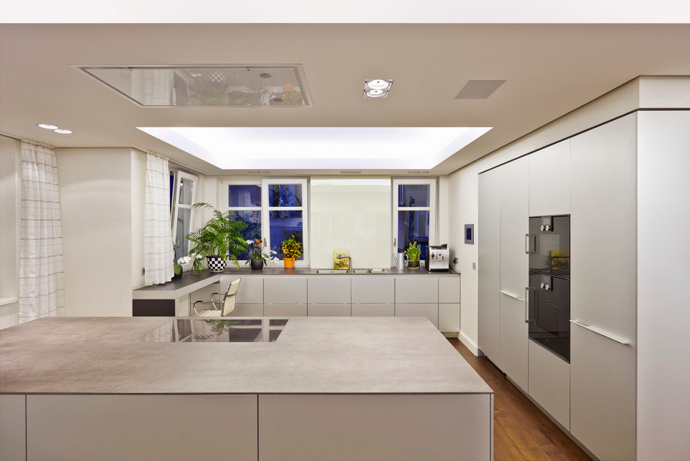 На фото: огромная отдельная кухня в современном стиле с двойной мойкой, плоскими фасадами, белыми фасадами, белым фартуком, фартуком из стекла, черной техникой, паркетным полом среднего тона и островом