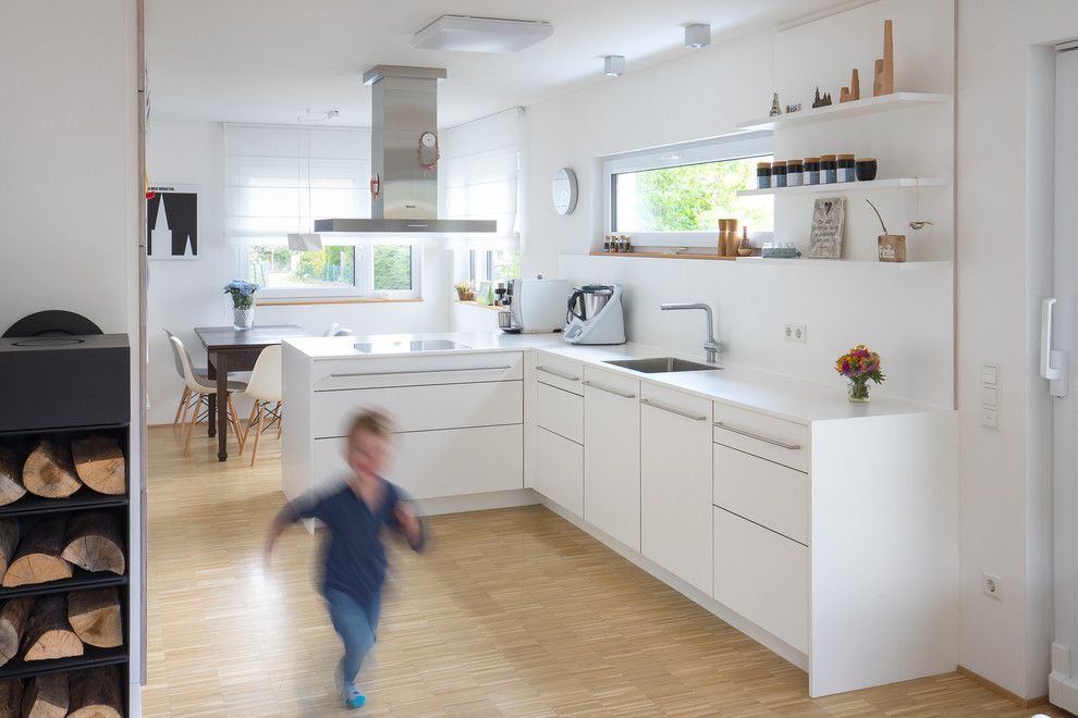 Modern inredning av ett mellanstort vit vitt kök, med en enkel diskho, släta luckor, vita skåp, laminatbänkskiva, vitt stänkskydd, stänkskydd i marmor, en halv köksö, bambugolv och beiget golv