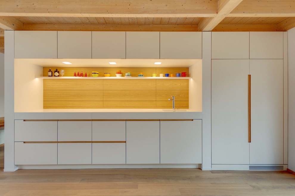 This is an example of a medium sized scandi single-wall open plan kitchen in Munich with flat-panel cabinets, white cabinets, an integrated sink, brown splashback and light hardwood flooring.