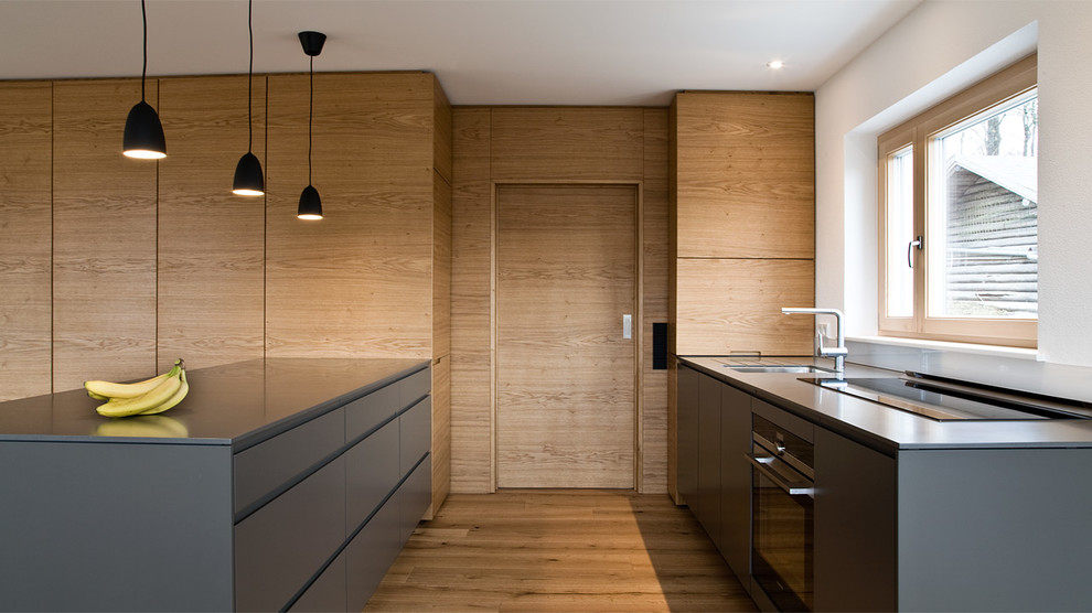 Exempel på ett stort modernt kök med öppen planlösning, med en undermonterad diskho, släta luckor, grå skåp, rostfria vitvaror, mellanmörkt trägolv, bänkskiva i rostfritt stål, vitt stänkskydd, glaspanel som stänkskydd och en halv köksö