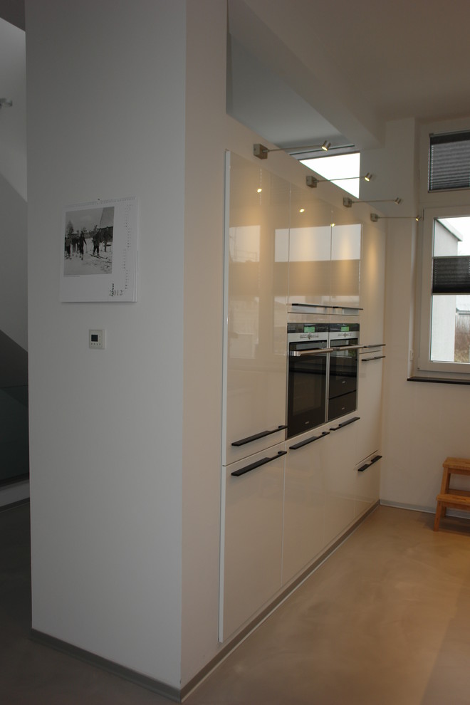 Large contemporary galley open plan kitchen in Essen with an integrated sink, flat-panel cabinets, white cabinets, composite countertops, white splashback, metro tiled splashback, stainless steel appliances, concrete flooring, an island and grey floors.