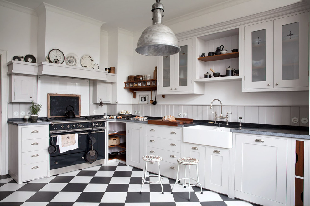 Bild på ett avskilt, stort lantligt l-kök, med en rustik diskho, skåp i shakerstil, vita skåp, grått stänkskydd och svarta vitvaror