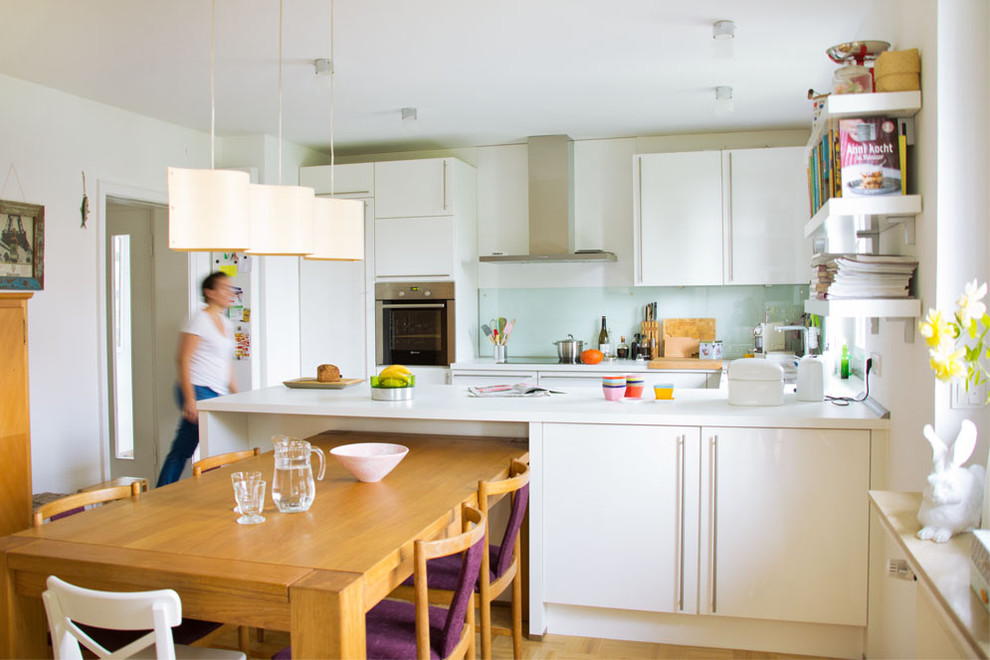 Foto på ett mellanstort minimalistiskt kök, med släta luckor, vita skåp, glaspanel som stänkskydd, vitt stänkskydd, integrerade vitvaror, mellanmörkt trägolv och en halv köksö