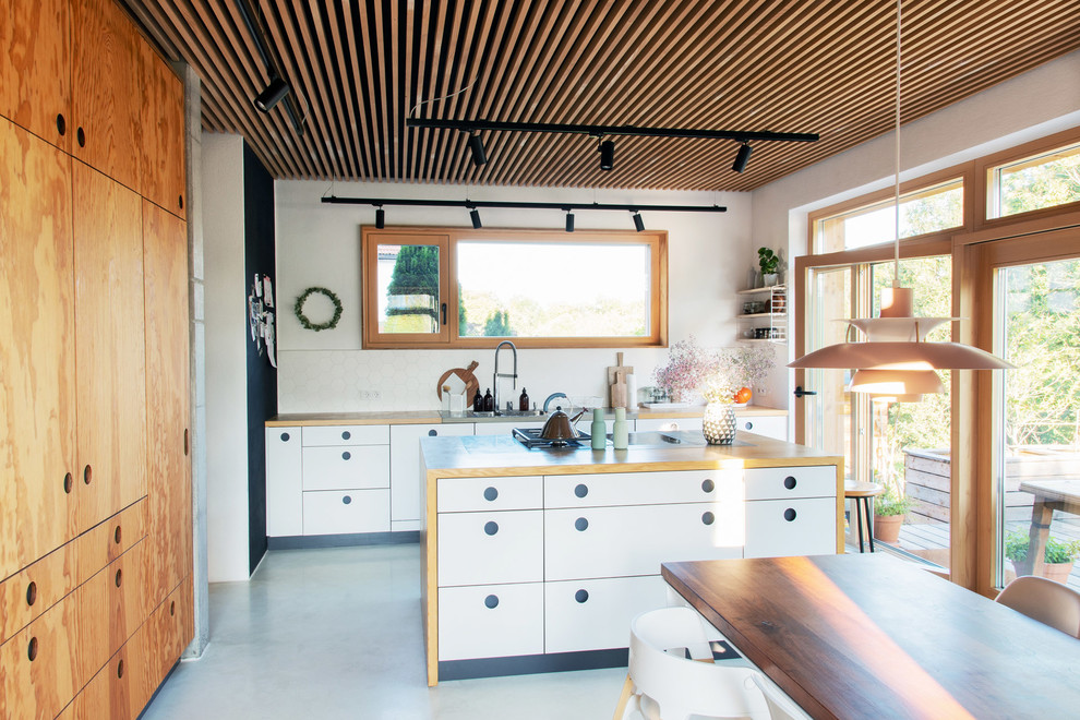 ミュンヘンにある北欧スタイルのおしゃれなキッチン (ドロップインシンク、フラットパネル扉のキャビネット、白いキャビネット、木材カウンター、白いキッチンパネル、コンクリートの床、グレーの床、茶色いキッチンカウンター) の写真