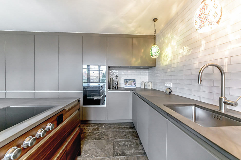 Inredning av ett mellanstort l-kök, med en integrerad diskho, släta luckor, grå skåp, vitt stänkskydd, stänkskydd i tunnelbanekakel, svarta vitvaror, marmorgolv och en köksö