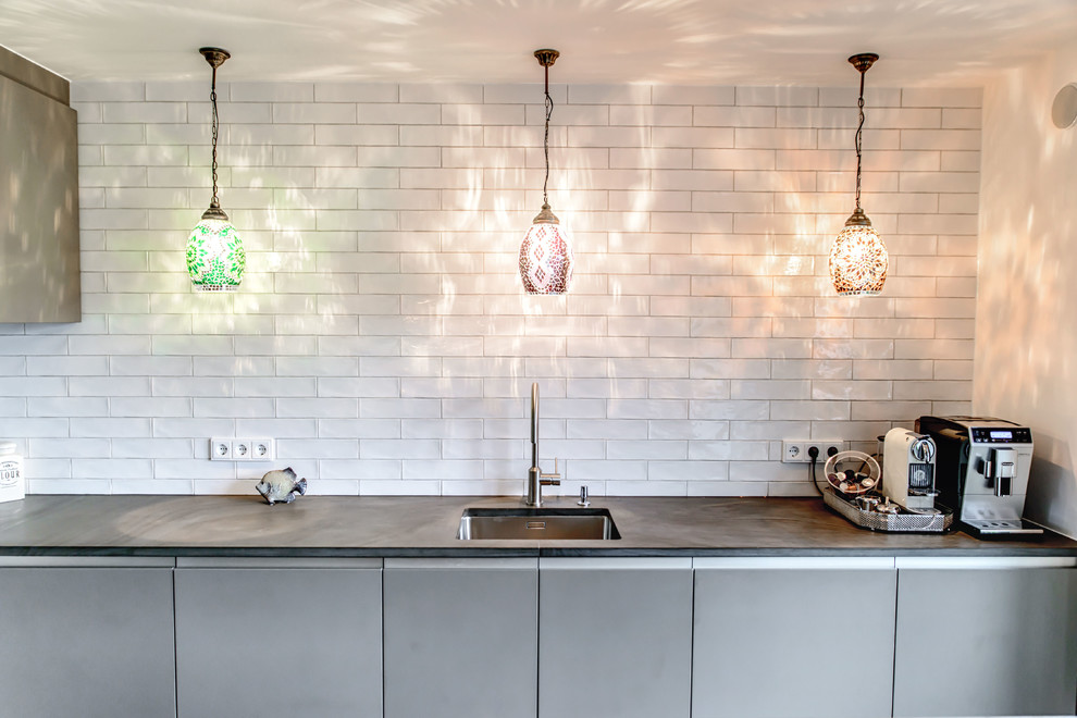 Moderne Küche mit integriertem Waschbecken, flächenbündigen Schrankfronten, grauen Schränken, Küchenrückwand in Weiß und Rückwand aus Metrofliesen in München