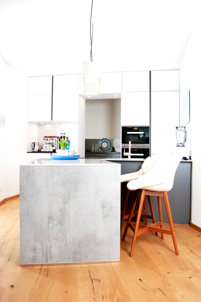 Bild på ett mellanstort funkis kök, med en enkel diskho, släta luckor, vita skåp, stänkskydd med metallisk yta, svarta vitvaror, mellanmörkt trägolv, en halv köksö och brunt golv