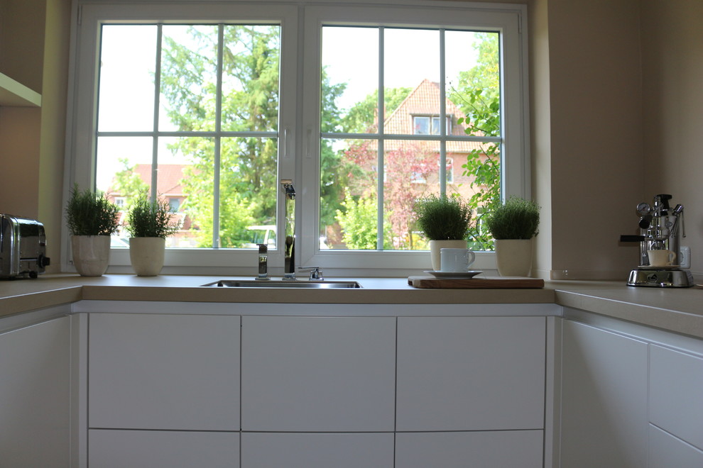Immagine di una grande cucina design con lavello integrato, ante bianche, paraspruzzi beige, paraspruzzi con lastra di vetro, elettrodomestici in acciaio inossidabile e pavimento con piastrelle in ceramica