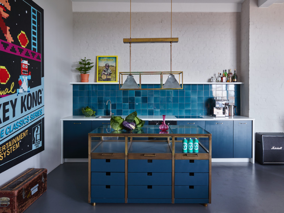Cette photo montre une petite cuisine linéaire éclectique avec un placard à porte plane, des portes de placard bleues, un plan de travail en verre, une crédence bleue, sol en béton ciré, îlot et fenêtre.