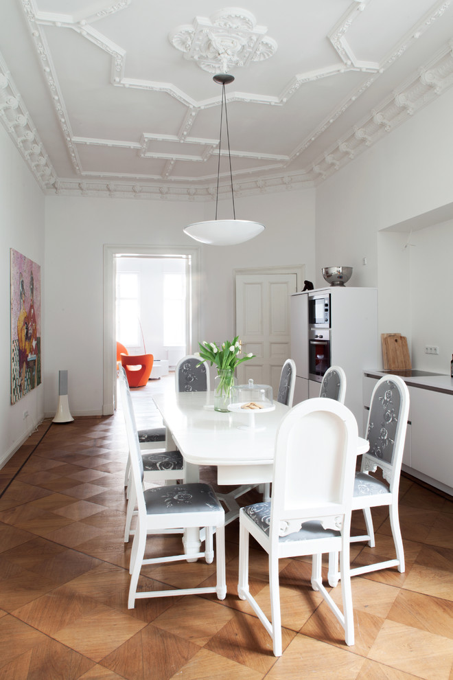 This is an example of a large eclectic single-wall kitchen/diner in Berlin with medium hardwood flooring, flat-panel cabinets, white cabinets, white splashback, stainless steel appliances and no island.