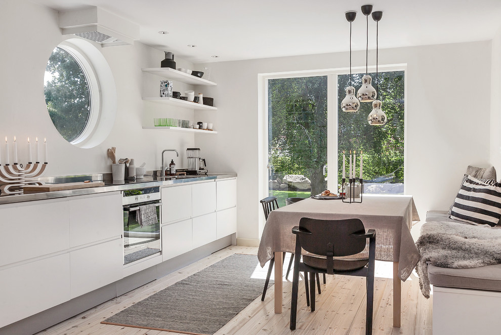 Idee per una cucina scandinava di medie dimensioni con ante lisce, ante bianche, paraspruzzi bianco, parquet chiaro, lavello a vasca singola, top in acciaio inossidabile e nessuna isola