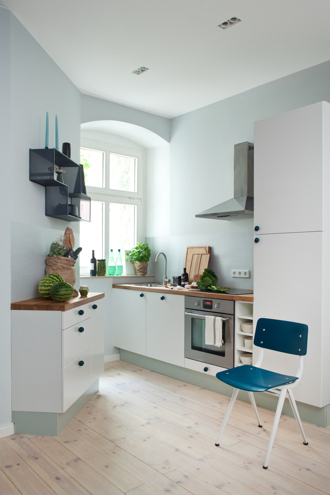 Inredning av ett modernt litet kök, med en undermonterad diskho, släta luckor, träbänkskiva, glaspanel som stänkskydd, ljust trägolv, vita skåp, blått stänkskydd och rostfria vitvaror