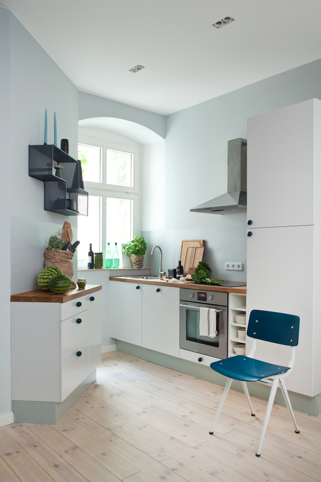 Kitchen - small contemporary light wood floor kitchen idea in Berlin with an undermount sink, flat-panel cabinets, wood countertops, glass sheet backsplash, no island, white cabinets, blue backsplash and stainless steel appliances