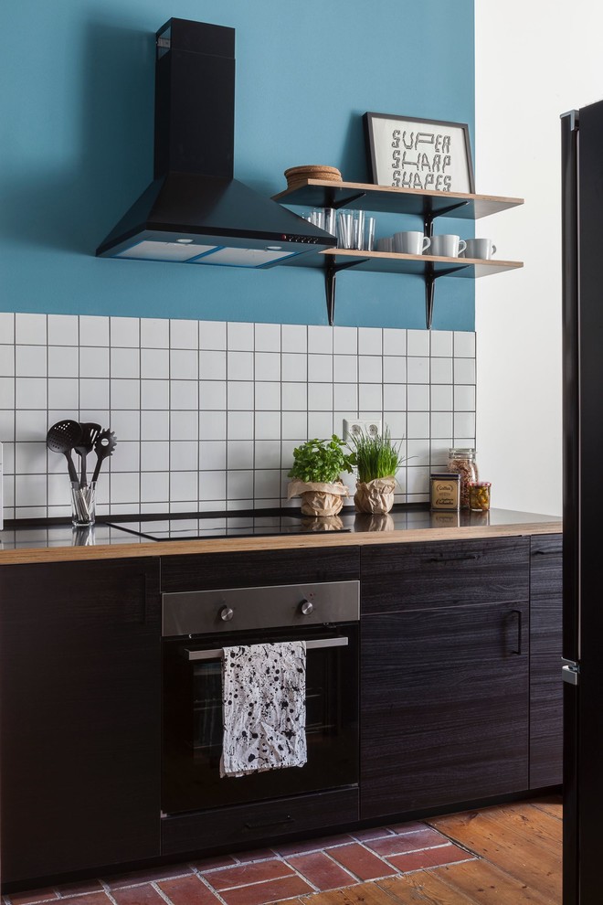 ベルリンにある小さなコンテンポラリースタイルのおしゃれなI型キッチン (フラットパネル扉のキャビネット、濃色木目調キャビネット、木材カウンター、白いキッチンパネル、セラミックタイルのキッチンパネル、黒い調理設備、無垢フローリング、アイランドなし、茶色い床、茶色いキッチンカウンター) の写真