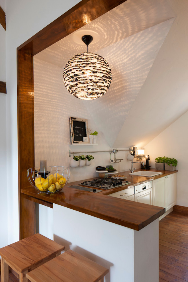 Photo of a small traditional single-wall kitchen in Frankfurt with a built-in sink, raised-panel cabinets, white cabinets, wood worktops, medium hardwood flooring, a breakfast bar, white splashback, integrated appliances and brown floors.