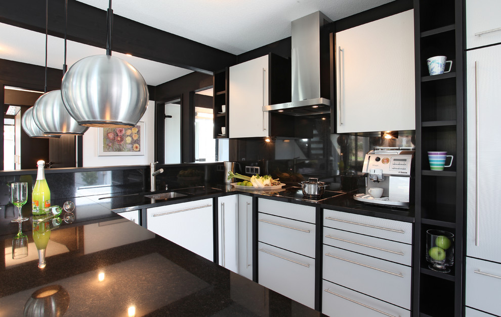 Cette image montre une cuisine design en U avec un évier encastré, un placard à porte plane, une crédence noire et un électroménager en acier inoxydable.