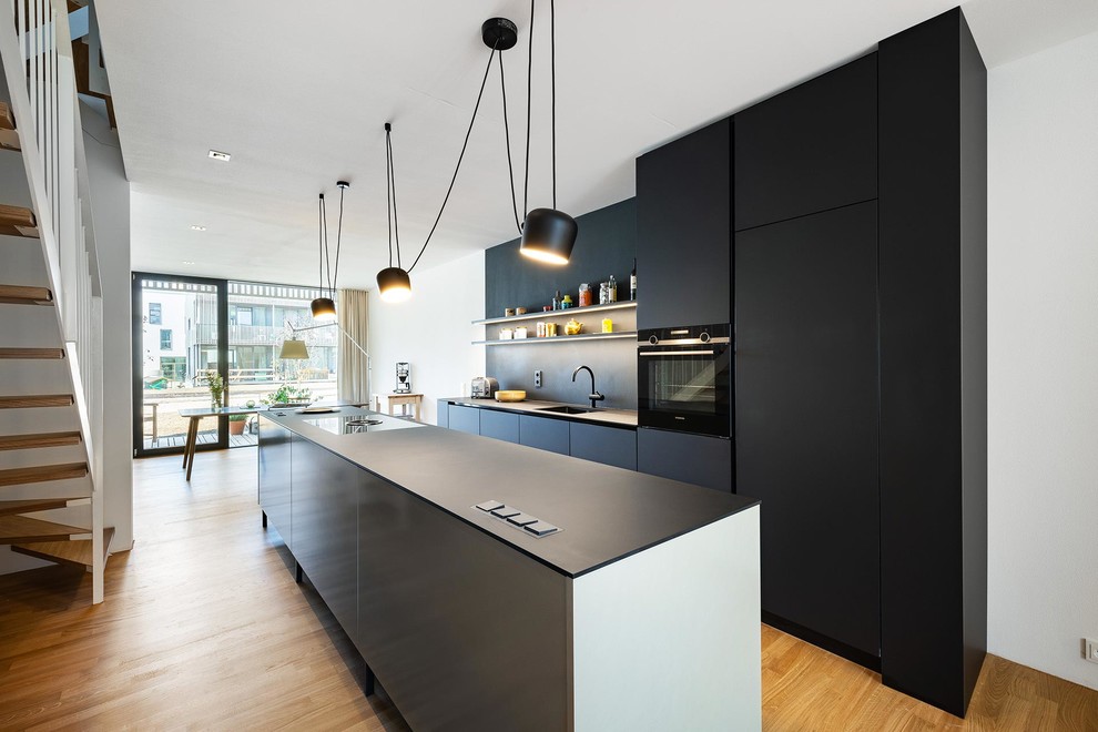 Inspiration för små moderna svart kök med öppen planlösning, med släta luckor, svarta skåp, svart stänkskydd, svarta vitvaror, en köksö och brunt golv