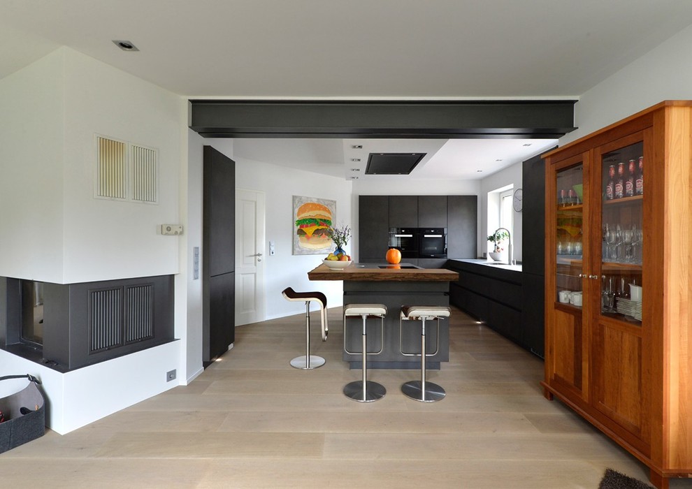 Photo of a medium sized contemporary galley open plan kitchen in Other with an integrated sink, flat-panel cabinets, grey cabinets, white splashback, black appliances, dark hardwood flooring, an island and brown floors.
