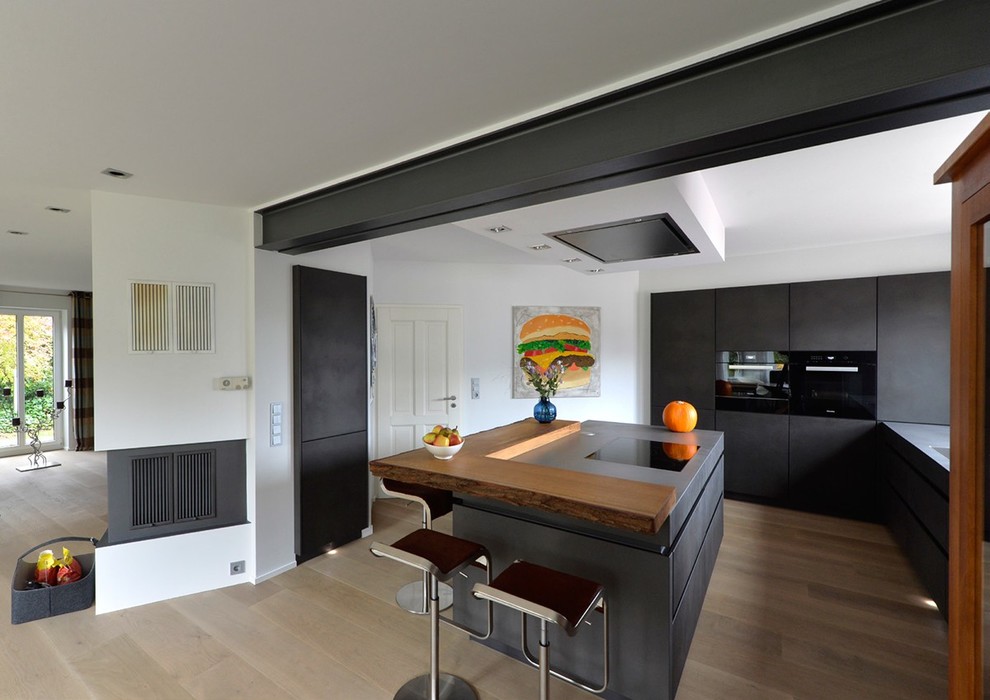 Cette photo montre une cuisine ouverte parallèle tendance de taille moyenne avec un placard à porte plane, des portes de placard grises, une crédence blanche, un électroménager noir, parquet foncé, îlot et un sol marron.