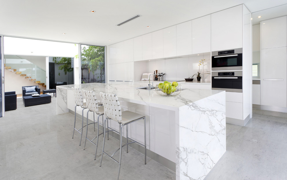 Modern inredning av ett stort kök med öppen planlösning, med en undermonterad diskho, släta luckor, vita skåp, vitt stänkskydd, en köksö, marmorbänkskiva och integrerade vitvaror