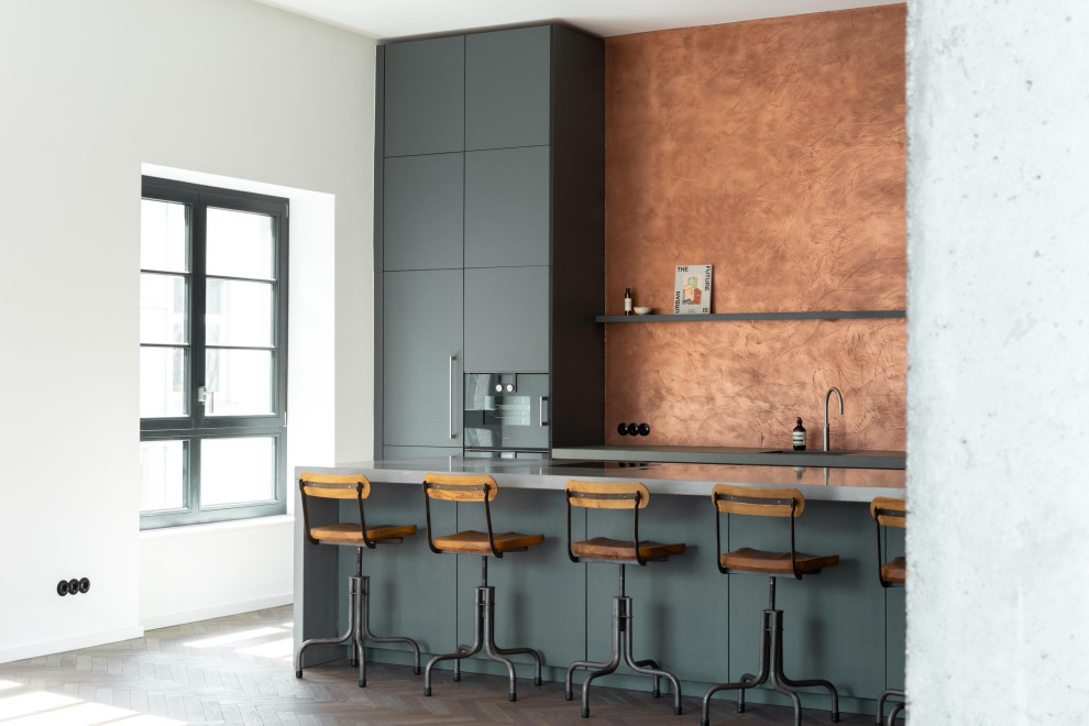 Bild på ett stort funkis grå linjärt grått kök och matrum, med en nedsänkt diskho, släta luckor, grå skåp, bänkskiva i betong, svarta vitvaror, mörkt trägolv och en köksö