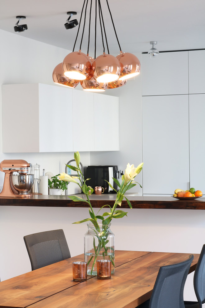 This is an example of a medium sized modern u-shaped kitchen/diner in Berlin with a built-in sink, flat-panel cabinets, white cabinets, composite countertops, white splashback, black appliances, bamboo flooring, no island and white floors.