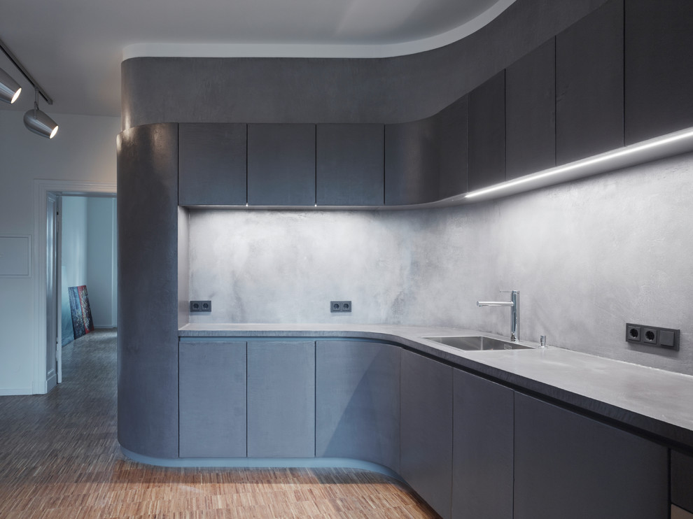 Foto på ett mellanstort funkis kök, med en nedsänkt diskho, grå skåp, bänkskiva i betong, grått stänkskydd, rostfria vitvaror, mellanmörkt trägolv och släta luckor