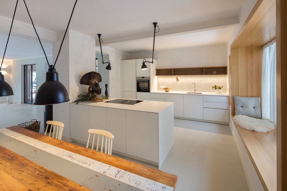 Open concept kitchen - mid-sized scandinavian galley white floor open concept kitchen idea in Berlin with white cabinets, an island, an integrated sink, flat-panel cabinets, beige backsplash, subway tile backsplash, black appliances and white countertops