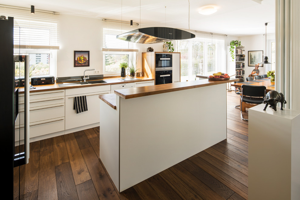 Moderne Wohnküche in L-Form mit Unterbauwaschbecken, flächenbündigen Schrankfronten, weißen Schränken, Arbeitsplatte aus Holz, dunklem Holzboden, Kücheninsel, braunem Boden und brauner Arbeitsplatte in Sonstige
