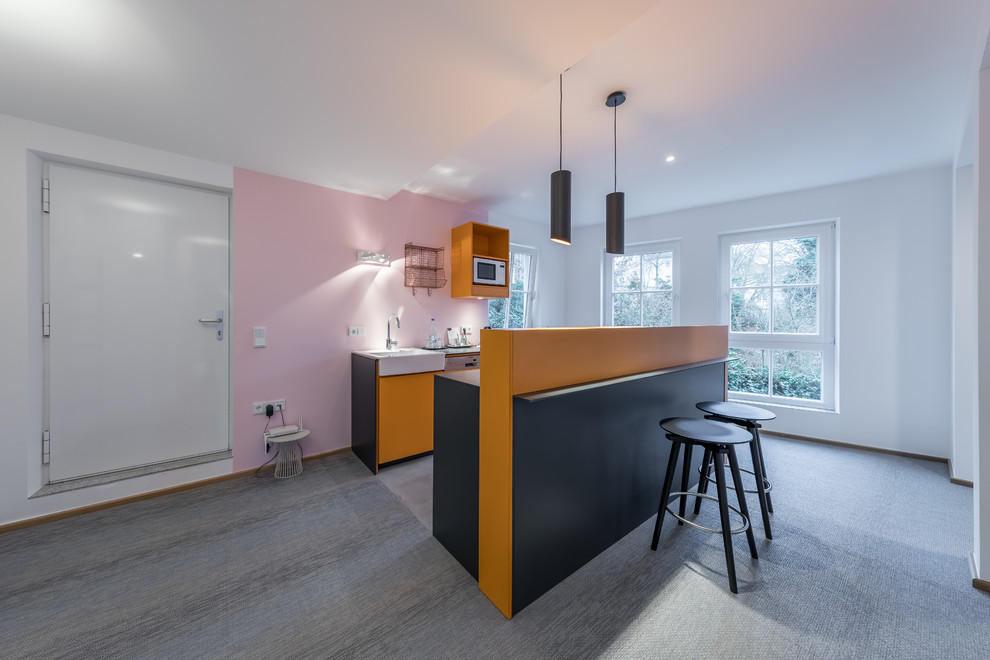 Exempel på ett litet modernt kök, med en integrerad diskho, släta luckor, orange skåp, laminatbänkskiva, rosa stänkskydd, glaspanel som stänkskydd, integrerade vitvaror, betonggolv, en köksö och grått golv