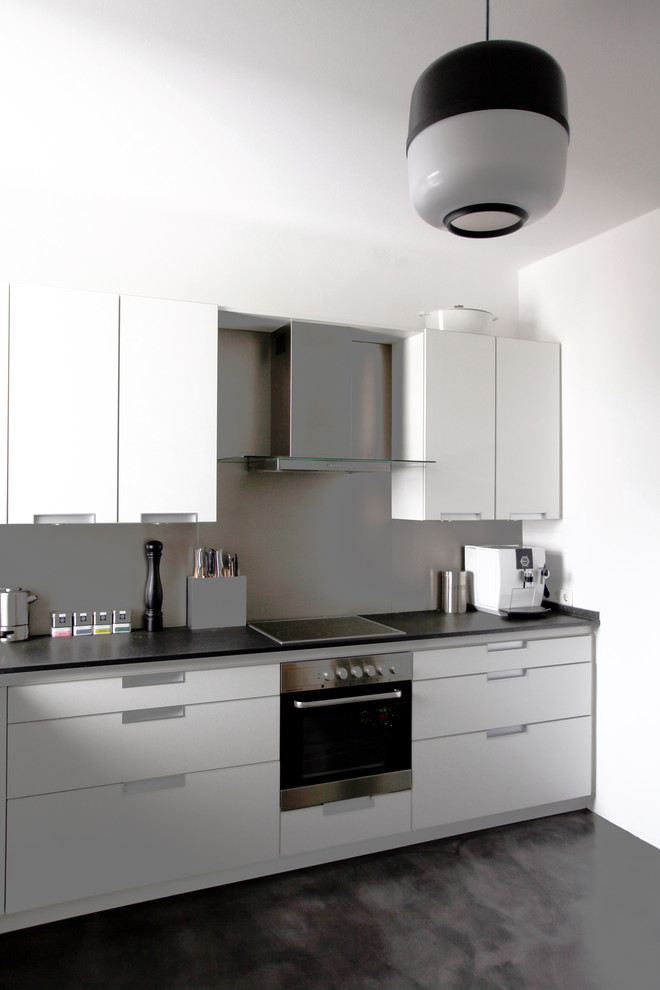 Foto på ett funkis linjärt kök, med släta luckor, vita skåp, stänkskydd med metallisk yta, rostfria vitvaror och svart golv