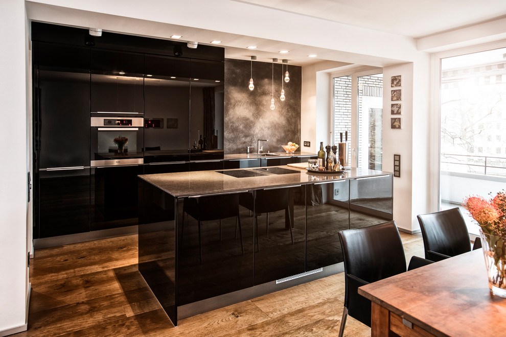 Einzeilige, Mittelgroße Moderne Wohnküche mit flächenbündigen Schrankfronten, schwarzen Schränken, bunter Rückwand, schwarzen Elektrogeräten, braunem Holzboden, Kücheninsel und braunem Boden in Düsseldorf