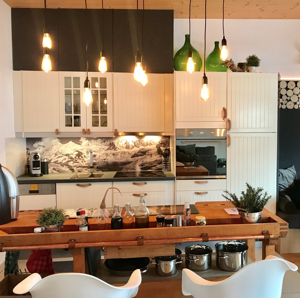 На фото: маленькая отдельная, параллельная кухня в стиле кантри с накладной мойкой, белыми фасадами, деревянной столешницей, разноцветным фартуком, черной техникой, полуостровом и плоскими фасадами для на участке и в саду