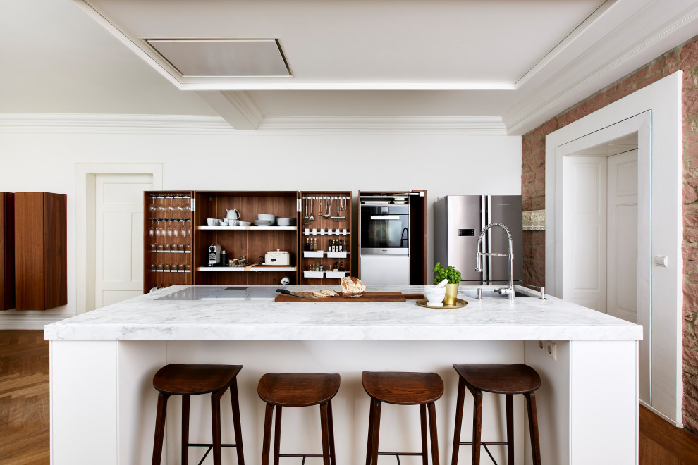 Foto di una grande cucina minimal con top in marmo, elettrodomestici in acciaio inossidabile, pavimento in legno massello medio, pavimento marrone, top bianco e lavello sottopiano