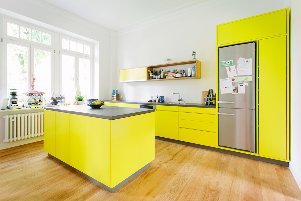 Offene, Zweizeilige Moderne grifflose Küche mit Einbauwaschbecken, flächenbündigen Schrankfronten, gelben Schränken, Küchenrückwand in Weiß, Küchengeräten aus Edelstahl, braunem Holzboden, zwei Kücheninseln und braunem Boden in Köln