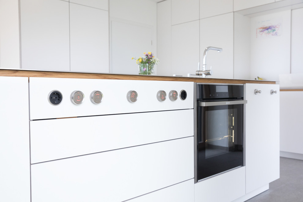 Foto på ett stort funkis grå linjärt kök med öppen planlösning, med en dubbel diskho, släta luckor, vita skåp, bänkskiva i rostfritt stål, vitt stänkskydd, rostfria vitvaror, en köksö, cementgolv och grått golv