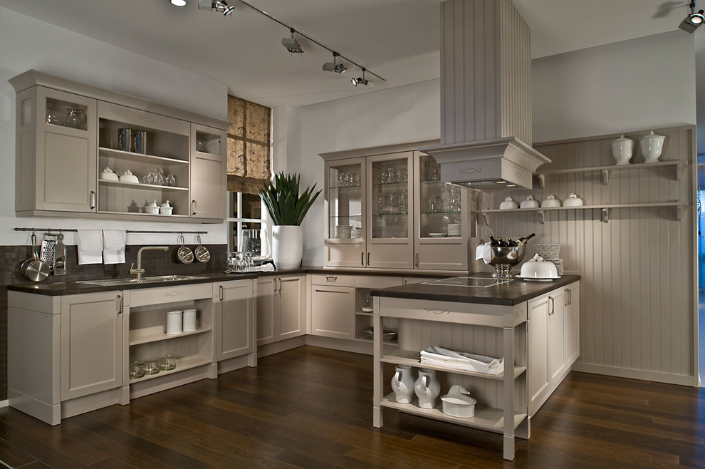 This is an example of an expansive rural u-shaped kitchen/diner in Bremen with a belfast sink, flat-panel cabinets, beige cabinets, wood worktops, beige splashback, stainless steel appliances, dark hardwood flooring and an island.