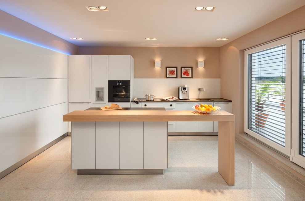 Immagine di una cucina design di medie dimensioni con ante lisce, ante bianche, top in legno, paraspruzzi bianco, elettrodomestici neri, lavello sottopiano, paraspruzzi con lastra di vetro e pavimento beige