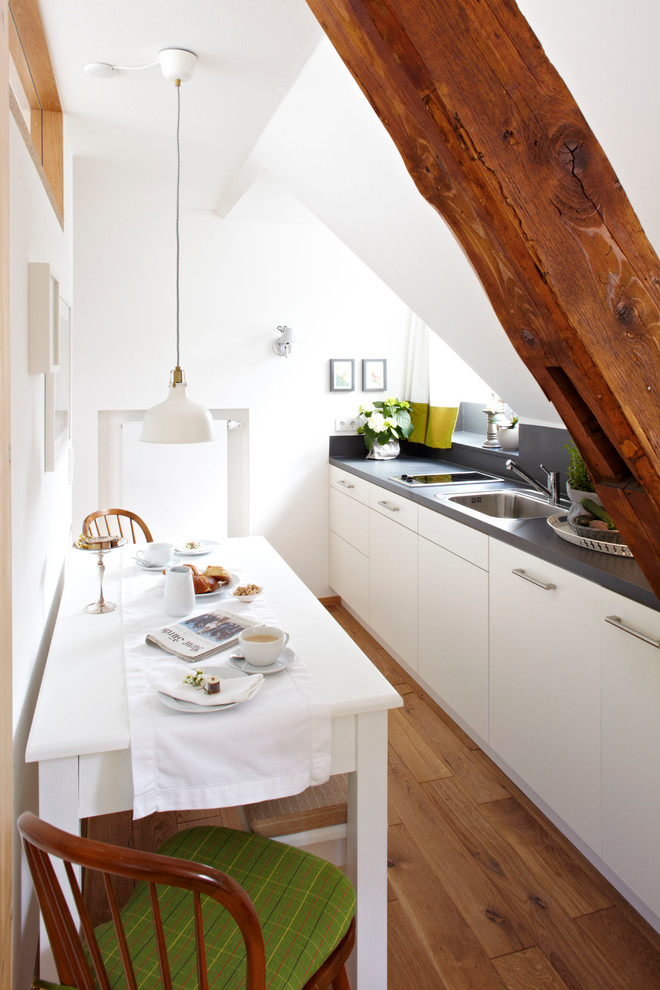 Inspiration for a small contemporary single-wall medium tone wood floor eat-in kitchen remodel in Munich with flat-panel cabinets, white cabinets, no island, a drop-in sink, gray backsplash and paneled appliances